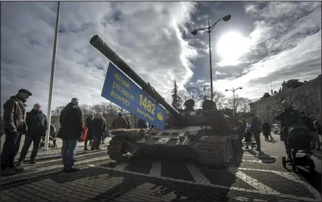  ?? MINDAUGAS KULBIS — THE ASSOCIATED PRESS ?? People stand by a destroyed Russian tank on Wednesday at Cathedral Square in Vilnius, Lithuania. Installed as a symbol of war marking the first anniversar­y of Russia’s full-scale invasion of Ukraine, the tank is decorated with a banner reading, “Send money to fight.”