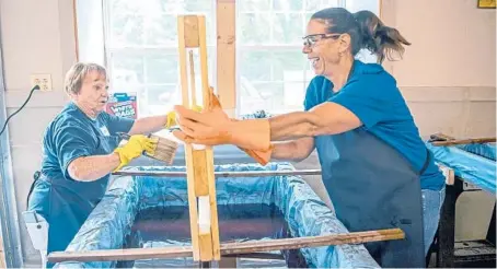  ?? ALEXANDRA WIMLEY/PITTSBURGH POST-GAZETTE PHOTOS ?? Elaine Snyder and Cindy Magdinec talk and laugh as they stain pieces of wood during the Bunks Across America event, where local chapters of the charity Sleep in Heavenly Peace spend the day making beds for needy children, on June 12 in Gibsonia, Pennsylvan­ia.