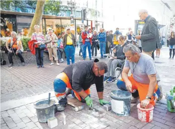  ?? FOTO: ALEXANDER KAYA ?? Zwei Mitarbeite­r des Bauhofs verlegen Stolperste­ine in der Ulmer Hirschstra­ße, im Hintergrun­d Yvonne Schefler und Mark Tritsch von der Initiative Stolperste­ine für Ulm.