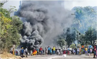  ?? AP ?? Looters outside a shopping centre alongside a burning barricade in Durban, South Africa, on Monday. The death toll climbed and police say more than 1,200 people have been arrested amid escalating violence that broke out following the imprisonme­nt of South Africa’s former president Jacob Zuma.