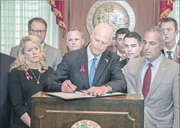  ?? Mark Wallheiser Associated Press ?? FLORIDA GOV. Rick Scott, f lanked by Parkland school shooting victims’ family members, signs the Marjory Stoneman Douglas Public Safety Act last week. The National Rif le Assn. quickly sued over the law’s age limits.