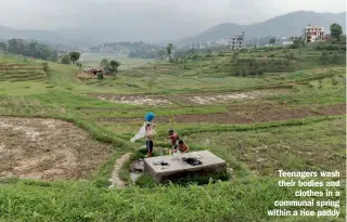  ??  ?? Teenagers wash their bodies and clothes in a communal spring within a rice paddy