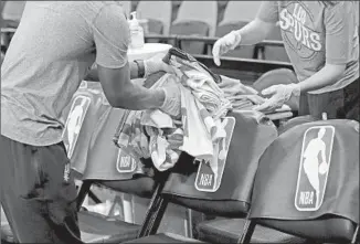  ?? Eric Gay Associated Press ?? TEAM ATTENDANTS use protective gloves Tuesday at AT&T Center in San Antonio, where the Spurs hosted the Dallas Mavericks. The NBA indefinite­ly suspended play Wednesday.