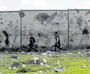  ?? Picture: FREDLIN ADRIAAN ?? PERPETUAL PROBLEM: Lee-Ann Johnson, 9, and Anam Masatie, 8, from Sedeberg Primary School in Booysen Park walk past a fence as the wind blows plastic bag refuse against it