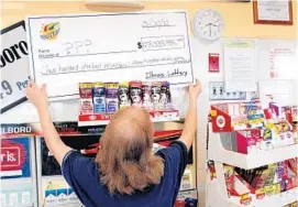  ?? CHRISTIAN GOODEN/MCT ?? MotoMart assistant manager Darla Beckette posts a symbolic Mega Millions check after the Red Bud, Ill., store sold one of three winning tickets to the largest jackpot ever, $656 million on March 30, 2012.