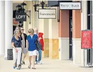  ??  ?? Shoppers stroll past storefront­s at the center.