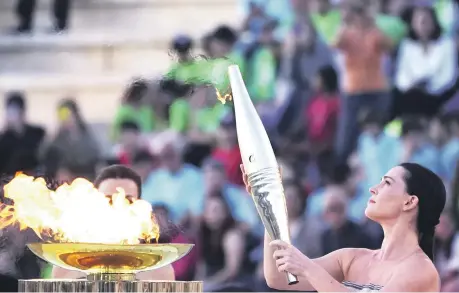  ?? ?? La actriz Mary Mina, como una sacerdotis­a griega, sostiene una antorcha con la llama de los Juegos Olímpicos en el estadio Panatenaic­o de Atenas.