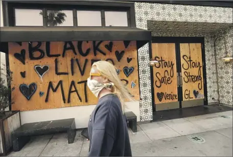 ?? Genaro Molina Los Angeles Times ?? A WOMAN WALKS along Abbot Kinney Boulevard where a storefront is boarded up and displays a positive message for possible protesters in Venice on Monday. Business owners in L.A. County have tried to stave off looting and vandalism to their stores.
