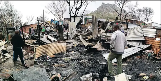  ?? Picture: HENK KRUGER ?? GUTTED: Residents of Imizamo Yethu in Hout Bay walk through the debris after a fire destroyed their homes over the weekend.