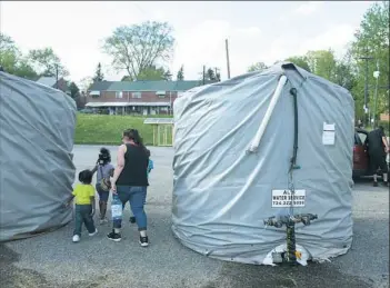  ?? Michael M. Santiago/Post-Gazette ?? Marie Kimball and her neighbor’s children retrieve water from a water buffalo after service was shut off Thursday in Century Townhomes in Clairton.