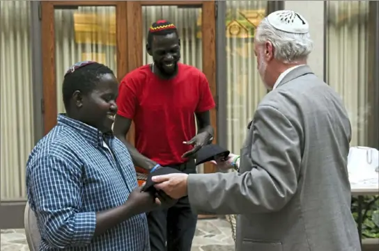  ?? Christian Snyder/ Post- Gazette ?? From left, Wanani Esau and Yonatan Katz Lukato receive gifts of yarmulkes from Tree of Life Rabbi Jeffrey Myers during a ceremony Monday at Rodef Shalom in Shadyside, which recognized the two Ugandan men’s congregati­on’s decision to rename itself Tree of Life.