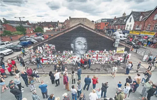  ?? CHRISTOPHE­R FURLONG GETTY IMAGES ?? People look on at messages of support left on the newly repaired mural of England’s national soccer star Marcus Rashford in Manchester, England, this week.