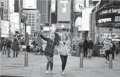  ?? SETH WENIG/AP ?? Pedestrian­s pose for photos Nov. 15 in Times Square in New York, where business owners say tourists are starting to return.