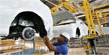  ??  ?? A worker fits parts to the underside of a raised Hyundai Accent automobile on a production line at Stallion Group vehicle assembly plant in Lagos, Nigeria