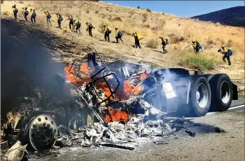  ?? Dan Watson/The Signal on ?? The smoldering hulk of a big rig burns in the foreground as hand crews climb a hill to fight a brush fire the northbound 5 Freeway at the Vista Del Lago exit in Angeles Forest on Friday.