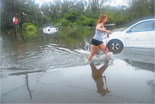  ?? JACK GRUBER/ USA TODAY ?? Mackenna Munson, 21, tries to get to her car Sunday on Rankin Street in Wilmington, N.C. Her family stayed through Hurricane Florence and weathered the storm without electricit­y. They woke up Sunday morning to find their street flooded.