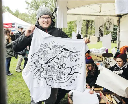  ?? PHOTOS: KERIANNE SPROULE ?? Mike Smyk, of Germany, holds up his new T-shirt, made with the help of Alberta Printmakin­g Society volunteers using the design of a new Calgary manhole cover at Prince’s Island Park on Saturday. Smyk is visiting Calgary from Frankfurt.