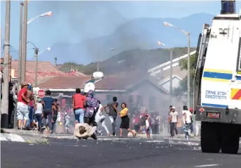  ?? — AFP photo ?? People run away as a South African Police Services armoured vehicle drives into a street during clashes with residents of Tafelsig, an impoverish­ed suburb in Mitchells Plain, near Cape Town.