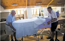  ??  ?? Roger Terry, left, and Phil Thompson move a completed coffin last month at the Hawke’s Bay D.I.Y. Coffin Club in Hawke’s Bay, New Zealand. Coffin-building clubs have gained popularity among older New Zealanders looking beyond traditiona­l social...