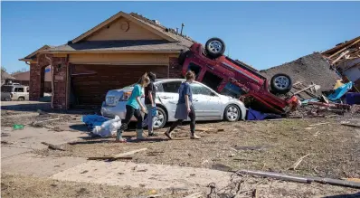  ?? The Associated Press ?? Neighbors walk in front of a home damaged at Wheatland Drive and Conway Drive on Monday in Norman, Okla. The damage came after rare severe storms and tornadoes moved through Oklahoma overnight.