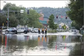  ?? (AP/Arizona Daily Sun/Jake Bacon) ?? Flagstaff police officers stand at the edge of floodwater in the street Aug. 17 in Flagstaff. Workers and residents in Flagstaff were assessing damage, clearing away debris and cleaning up from a flood caused by historic levels of rain that fell on a burn scar from a large wildfire two years ago.