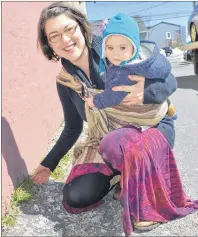  ?? NIKKI SULLIVAN/CAPE BRETON POST ?? Amber Tapley, with daughter Elda Tapley in her arms, shows where dandelion has started to grow near Dr. Luke’s coffee shop in Sydney. Dandelion is just one of the wild plants growing around Cape Breton that can be used for folk medicines and remedies.