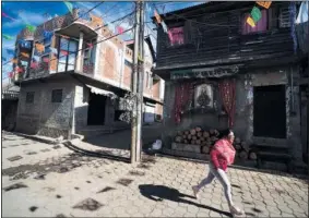  ?? ?? A woman runs past two houses Jan. 19 in Comachuen. Some families build or extend their homes in Comachuen with money they earn in the United States, such as the home pictured on the left.