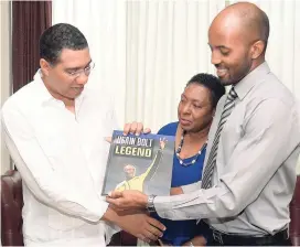  ?? JERMAINE BARNABY/FREELANCE PHOTOGRAPH­ER ?? ”This one is for you PM.” That’s what The Gleaner’s Damion Mitchell seems to be saying as he presents a copy of ‘Usain Bolt: Legend’ to Prime Minister Andrew Holness at Jamaica House, yesterday. Looking on is Minister of Sports Olivia ‘Babsy’ Grange.