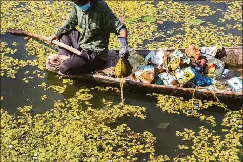  ?? Mukhtar Khan / Associated Press ?? A Kashmiri boatman employed by the Lakes and Waterways Developmen­t Authority removes garbage from the Dal Lake in Srinagar, Indian controlled Kashmir, Sept. 14, 2021. Dal Lake appears pristine in the area where hundreds of exquisitel­y decorated houseboats bob on its surface for rent by tourists and honeymoone­rs. But farther from shore, the lake is a mixture of mossy swamps, thick weeds, trash-strewn patches and floating gardens made from rafts of reeds.