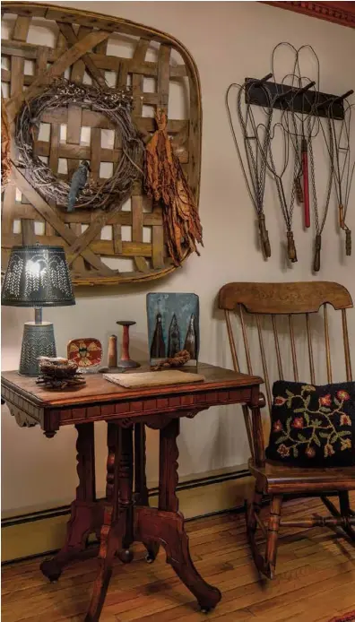  ??  ?? To liven up the living room, Jan crowns an Eastlake table with a tobacco basket adorned with a grapevine wreath and dried tobacco leaves. Above the heirloom rocking chair, she displays rug beaters on a wood peg rack. “Our home is filled with items that stir childhood memories. Many objects I used growing up,” Jan says.