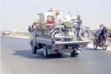  ??  ?? Syrian children riding in the back of a truck loaded with furniture and a motorcycle, driving along the main Damascus-Aleppo highway, as families flee north from the countrysid­es of of Hama and Idlib provinces from government forces bombardmen­t.
