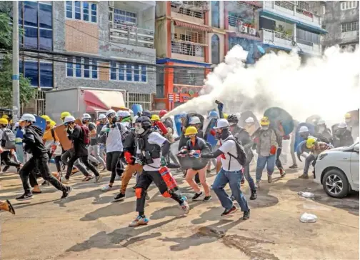  ?? Associated Press ?? Anti-coup protesters run as one of them discharges a fire extinguish­er to counter the impact of tear gas fired by riot policemen in Yangon, Myanmar on Wednesday.