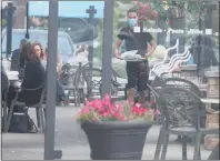  ??  ?? A server carries away plates at Bostons on Hall Road on Sunday. Outdoor dining has helped several Macomb County eateries survive.