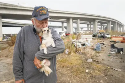  ?? Paul Chinn / The Chronicle ?? Kelly Thompson snuggles with his dog, Elvira, before moving out of a homeless encampment on Oakland’s Wood Street, where he lived for a year until city officials began clearing it to create a safe parking lot in November.