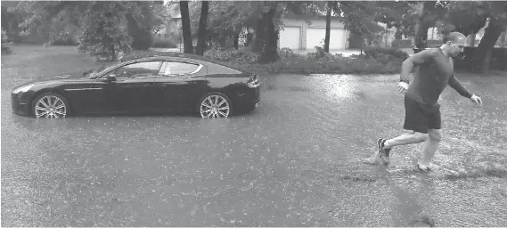  ?? DAN JANISSE ?? A man walks away from his Aston Martin on Riverside Drive East near Jefferson Boulevard on Thursday after it stalled in the flooded street.