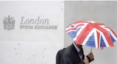  ?? — Reuters ?? A worker shelters from the rain as he passes the London Stock Exchange in the city of London.