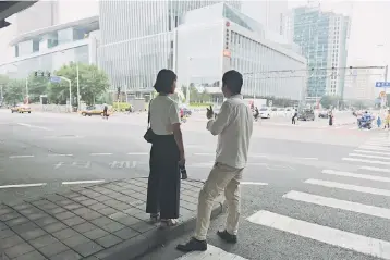  ??  ?? A couple waits to cross a road in Beijing’s central business district on July 12. Most US businesses operating in China oppose the use of tariffs in retaliatio­n for the challenges they face, from an uneven playing field to poor protection of...
