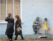  ?? EFREM LUKATSKY THE ASSOCIATED PRESS ?? People pass by an image from the famous street artist TvBoy, created on a wall of the house of culture, which was heavily damaged during Russia’s attack in the town of Irpin, outside Kyiv.