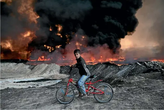  ?? GETTY IMAGES ?? An Iraqi boy rides his bicycle past an oilfield set on fire by retreating Islamic State fighters. Isis has attacked the oil hub of Kirkuk to try to relieve the pressure on Mosul.