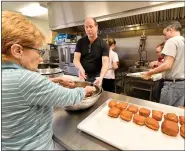  ??  ?? Betty Hoffman receives a bowl of fried fasnachts to be placed on cooling trays from Craig Bogia on Saturday at Friedens United Church of Christ in Oley. Both are residents of Ruscombman­or Township.