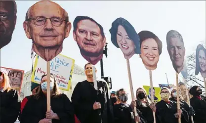  ?? Gabriela Bhaskar/The New York Times ?? People hold signs featuring faces of Supreme Court justices, during a rally in front of the Supreme Court in Washington on Dec. 1, as the court hears a case that concerns a Mississipp­i law that bans most abortion after 15 weeks of pregnancy, about two months earlier than Roe v. Wade allows.