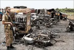  ?? IRAM ASIM/AP ?? A Pakistani soldier stands guard Sunday as workers inspect the site of an explosion.