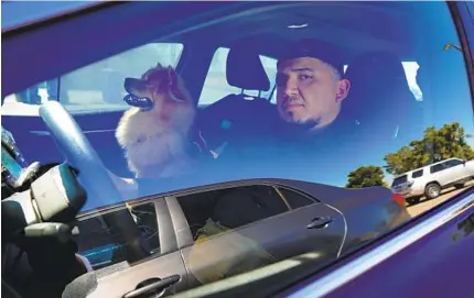  ?? NELVIN C. CEPEDA U-T ?? Jonathan Renteria, with his dog, Appa, sits in his car in the parking lot of Southweste­rn College. The Toyota Camry was his home for about a month last fall as he struggled financiall­y after losing his two jobs due to the pandemic.