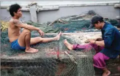  ?? NICOLAS ASFOURI/AFP ?? Migrant workers repair a net on a Thai fishing boat in Thailand’s Rayong province. Two Cambodian migrants trafficked from Thailand onto a Malaysian vessel returned home yesterday.