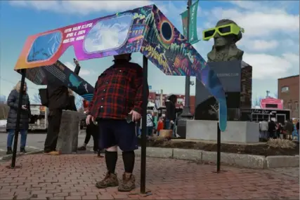  ?? Joe Raedle/Getty Images ?? Visitors look through a pair of oversized eclipse glasses set up in the town square Sunday in Houlton, Maine. Millions of people have flocked to areas across North America that are in the “path of totality” in order to experience a total solar eclipse.