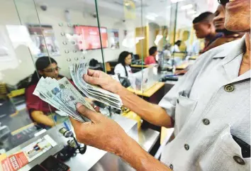  ?? Virendra Saklani/Gulf News Archives ?? Customers transact at a UAE Exchange branch in Sharjah, in this file picture. The company halted all transactio­ns when monetary authoritie­s launched a probe into its operations.