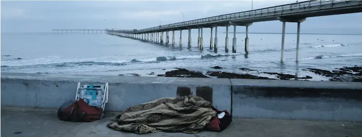  ??  ?? A person sleeps under a blanket on a beach near the Ocean Beach Pier in San Diego. There is a US$531 million plan underway that would take 2,700 people off the street through new constructi­on or refurbishi­ng of hotels over the next five years. Federal,...