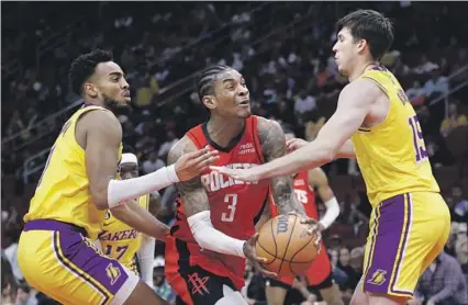  ?? Carmen Mandato Getty Images ?? THE ROCKETS’ Kevin Porter Jr. splits Lakers defenders Troy Brown Jr., left, and Austin Reaves as he drives to the basket during the first half. Reaves led the Lakers with 24 points off the bench in Houston’s 114-110 victory. The Lakers fell two games below .500.