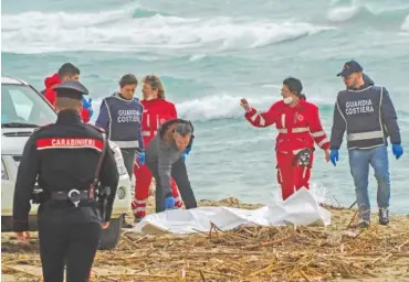  ?? PHOTOS BY ANTONINO DURSO/LAPRESSE VIA AP ?? Italian Red Cross volunteers and coast guards recover a body after a migrant boat broke apart in rough seas Sunday at a beach near Cutro, southern Italy.
