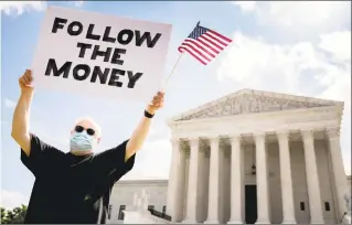  ?? Andrew Harnik / Associated Press ?? Bill Christeson holds up a sign that reads “Follow the Money” outside the U.S. Supreme Court on Thursday. The Supreme Court ruled Thursday that the Manhattan district attorney can obtain Trump tax returns while not allowing Congress to get Trump tax and financial records, for now, returning the case to lower courts.